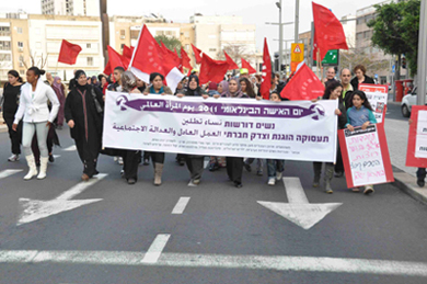 The streets of Tel Aviv could not remain indifferent to the energy of dozens of working and unemployed women, both Jewish and Arab, who marched along a central chic boulevard on International Women’s Day 2011. As they marched, the women shouted slogans in Hebrew and Arabic calling for fair employment, condemning unemployment and poverty, expressing solidarity with the social workers (who have been in an ongoing labor dispute), and demanding both “bread and roses.” 